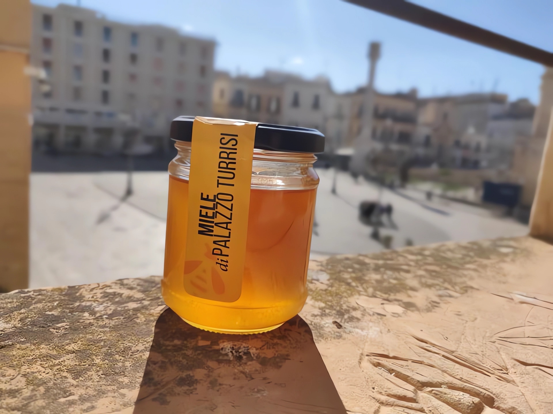 Vasetto di miele dell'apiario Turrisi con lo sfondo della piazza di Sant'Oronzo Lecce
